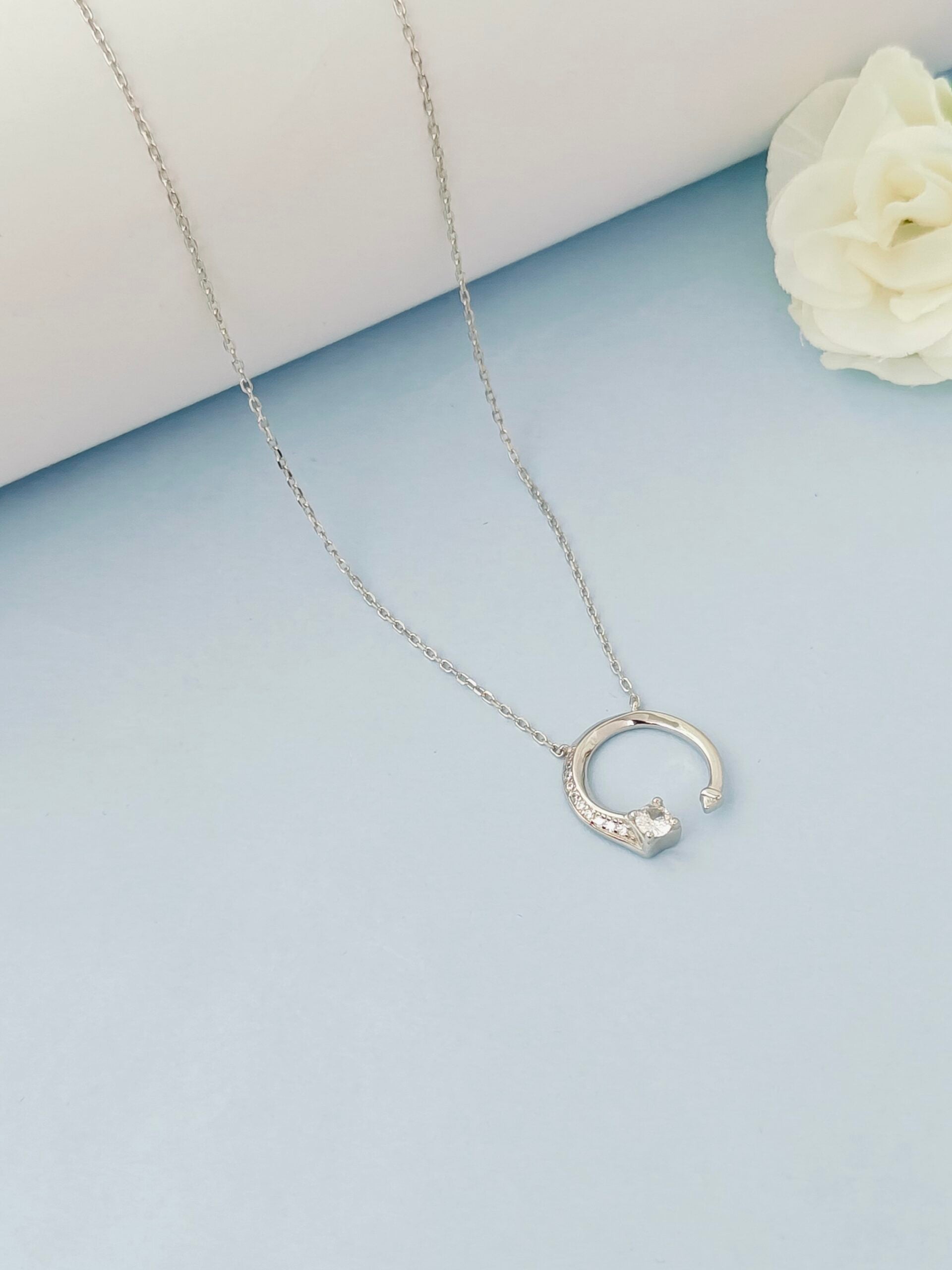 Silver necklace with a crescent moon pendant on a light blue surface with a white flower.